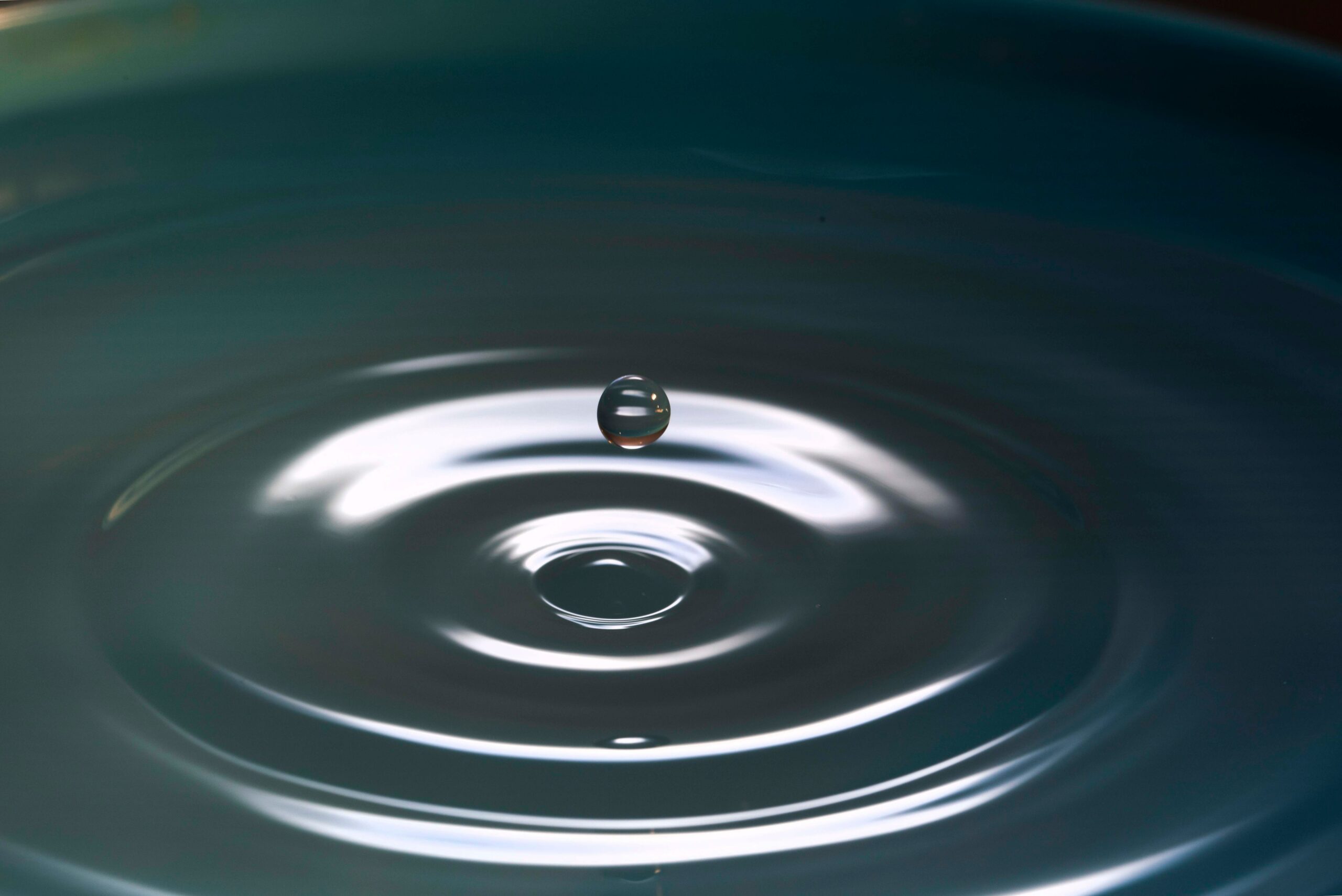Water droplet creating concentric ripples on surface